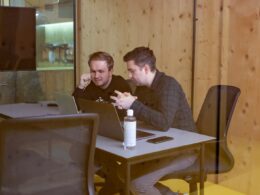 two men sitting at a table with a laptop