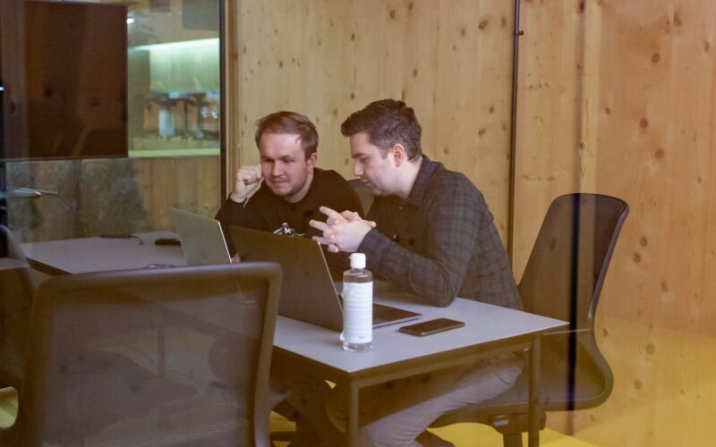 two men sitting at a table with a laptop
